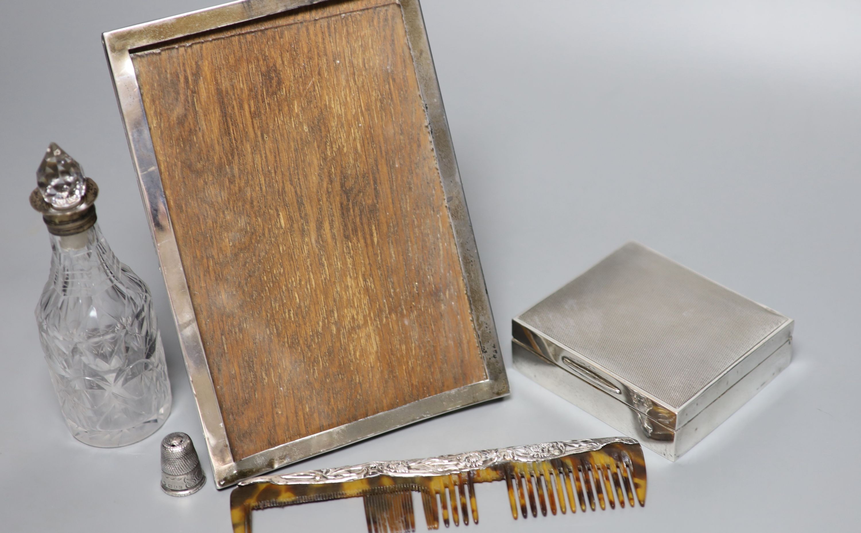 A silver mounted cigarette box, a silver mounted photograph frame, a silver thimble, a silver mounted comb(a.f.) and a silver mounted glass condiment bottle.